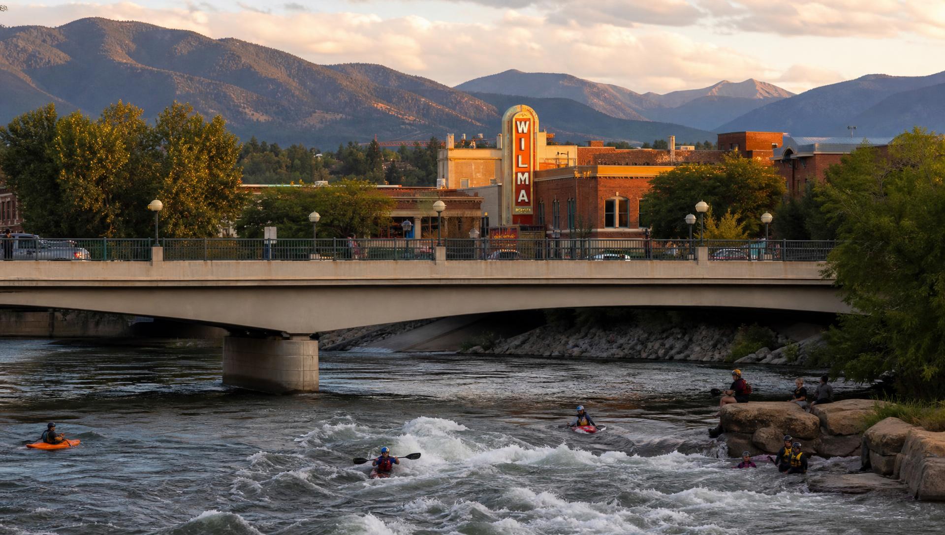 The Higgins Avenue Bridge over the Clark Fork River in downtown Missoula at golden hour, with the Wilma sign and mountains behind